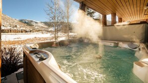 A hot tub with steam rising, surrounded by a wooden deck and a snowy landscape in the background.
