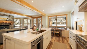 A spacious kitchen with a large island, wooden beams, and a stone fireplace.