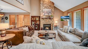 A cozy living room with a stone fireplace, comfortable seating, and a large window with blinds. - Family & Pet Retreat-2 Amazing Game Rooms-FencedYd-Pool-Beach-JimThorpe-Speedway (Albrightsville)