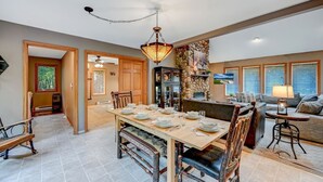A spacious dining area with a long table set for four, surrounded by wooden chairs. A stone wall and a fireplace are visible in the background. - Family & Pet Retreat-2 Amazing Game Rooms-FencedYd-Pool-Beach-JimThorpe-Speedway (Albrightsville)