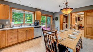 A modern kitchen with wooden cabinets, a dishwasher, and a dining area with a table set for four. - Family & Pet Retreat-2 Amazing Game Rooms-FencedYd-Pool-Beach-JimThorpe-Speedway (Albrightsville)