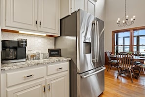 A kitchen with white cabinets, a stainless steel refrigerator, a coffee maker, and a sign that reads "Coffee Bar".