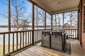 A covered deck with wicker furniture and a view of a lake.
