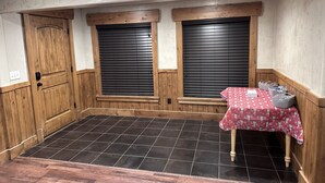 Une pièce avec une porte en bois, deux fenêtres équipées de stores, une table recouverte d’une nappe rouge et des paniers en osier.