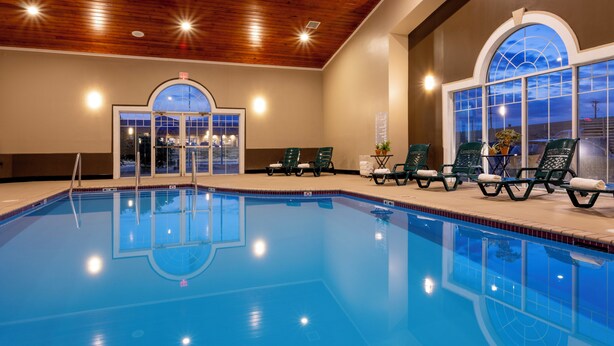 An indoor swimming pool with clear blue water, surrounded by lounge chairs and a wooden ceiling. - GrandStay Hotel & Suites - Waunakee  (Waunakee)