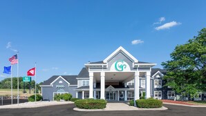 A hotel with a prominent 'GrandStay' sign, a covered entrance, and multiple flags including the American flag. - GrandStay Hotel & Suites - Waunakee  (Waunakee)