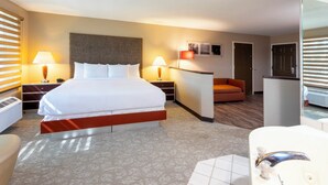 A hotel room with a large bed, two bedside tables with lamps, a desk with a chair, a small sofa, and a bathroom with a sink and mirror. - GrandStay Hotel & Suites - Waunakee  (Waunakee)