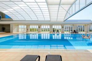 An indoor swimming pool with clear glass ceilings, lounge chairs, and a view of the outdoors. - Boavista Golf and Spa Resort - Bayview (Lagos)