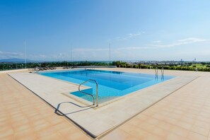 A rectangular swimming pool with a metal ladder on one side, surrounded by a tiled deck.