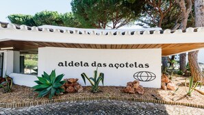 Ein Schild mit dem Text "aldeia das açoteiras", umgeben von Pflanzen und Steinen.