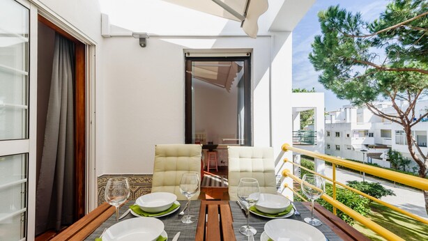 Ein Balkon mit Essbereich, inklusive Tisch, Stühlen und Blick auf die umliegenden Gebäude und Grünflächen.