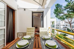 Een balkon met een eettafel, stoelen en uitzicht op de omliggende gebouwen en groen.