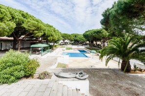 A courtyard with a swimming pool, surrounded by trees and covered seating areas. - Aldeia das A Oteias Apartment (Albufeira)