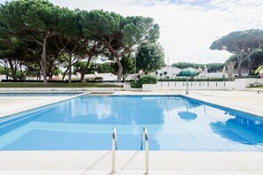 A rectangular swimming pool with two metal ladders, surrounded by a white wall and trees. - Aldeia das A Oteias Apartment (Albufeira)