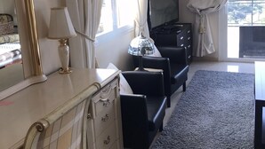 A hotel room with a large window, a flat-screen TV, a sofa, a desk with a lamp, and a dresser. - Coast View Villa (Marbella)