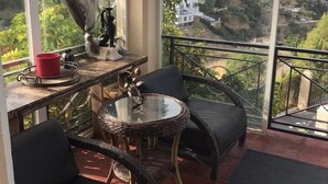 A balcony with wicker furniture, a table with a red cup, and a view of a hillside with buildings. - Coast View Villa (Marbella)