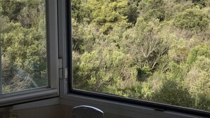 A view from a window overlooking a hilly landscape with dense greenery and a distant building complex. - Coast View Villa (Marbella)