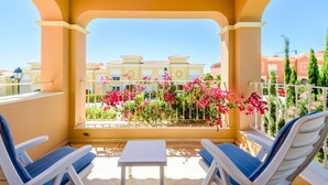 A balcony with two lounge chairs and a small table, overlooking a building with balconies and pink flowers. - Casa Mapie - Boavista Golf Resort Spa (Lagos)