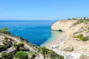Vista costera con playa, mar azul cristalino y acantilados rocosos.