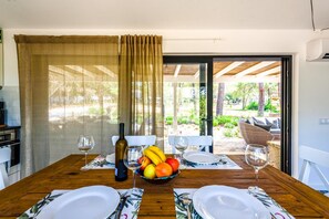 A dining table set for two with a bottle of wine, a bowl of fruit, and a view of the garden through the glass door. - Casa dos Sonhos in Vale do Lobo (Loulé)