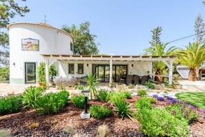 A white building with a covered patio area, outdoor seating, and a garden with various plants and flowers. - Casa dos Sonhos in Vale do Lobo (Loulé)