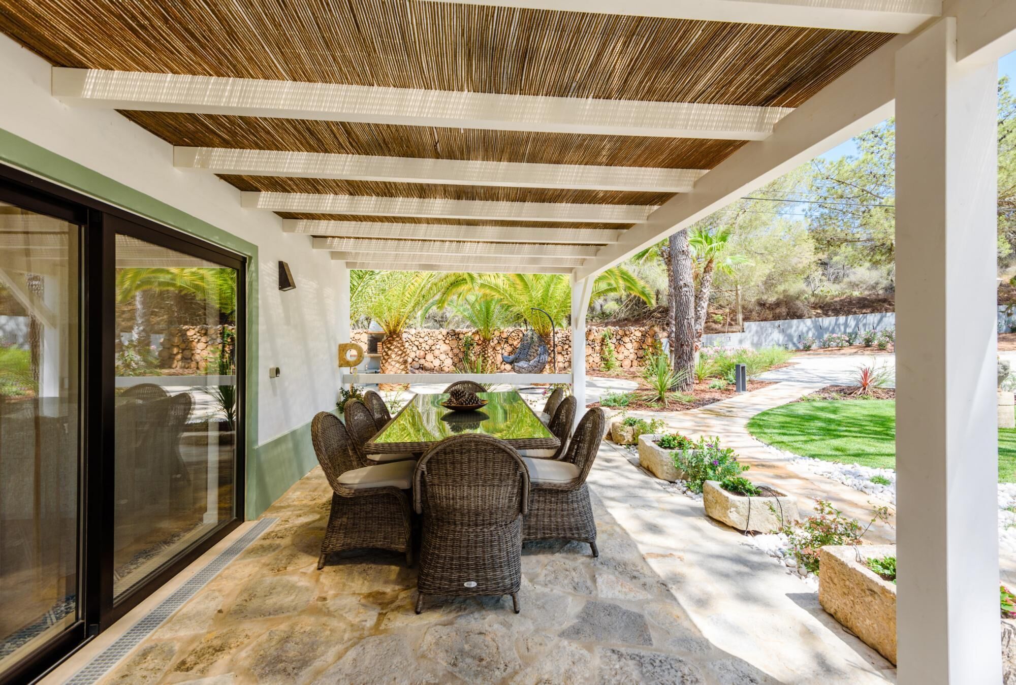 Un patio al aire libre con una mesa y sillas para comer, rodeado de suelo de piedra y una pérgola.