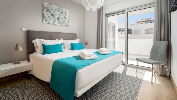 A modern hotel room with a large bed, a view through the glass door, and a chair by the window. - Lagos Town Centre Apartment (Lagos)