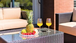 A glass-top table with a fruit platter, two glasses of orange juice, and wicker furniture on an outdoor patio. - L Orangerie in Vilamoura (Loulé)