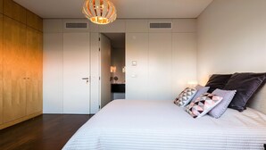 A bedroom with a large bed, wooden wardrobe, and a modern pendant light. - L Orangerie in Vilamoura (Loulé)