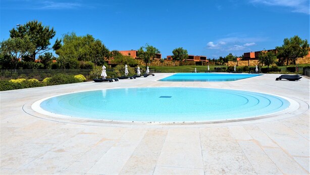 A large outdoor swimming pool with a circular design, surrounded by a paved area and a fence. - L Orangerie in Vilamoura (Loulé)
