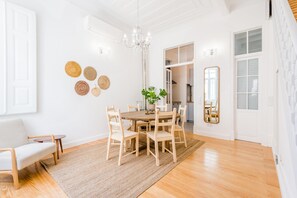 Un comedor con una mesa redonda de madera, seis sillas, una araña y un espejo en la pared.
