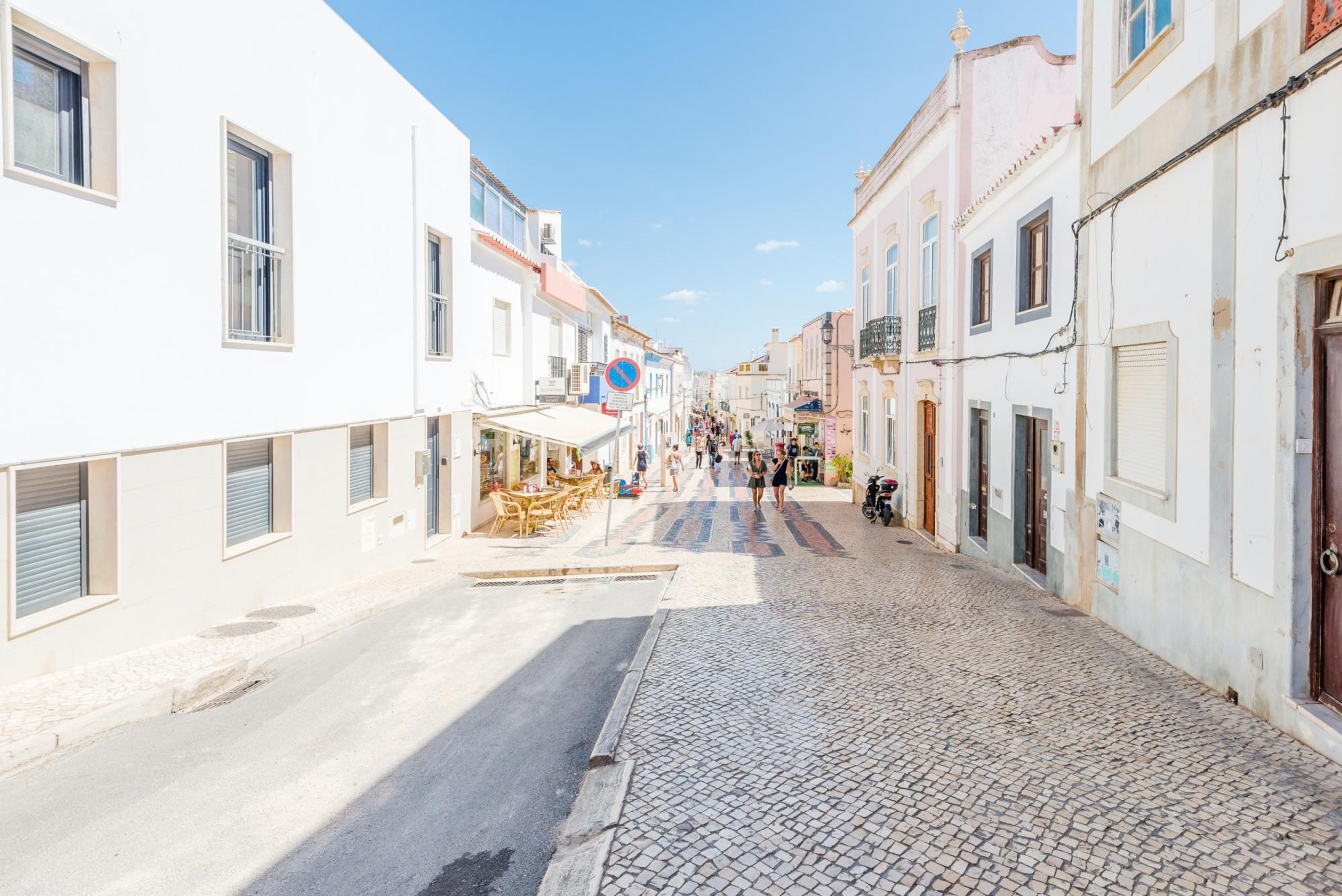Uma rua de paralelepípedos ladeada por edifícios, alguns com persianas e outros com varandas.