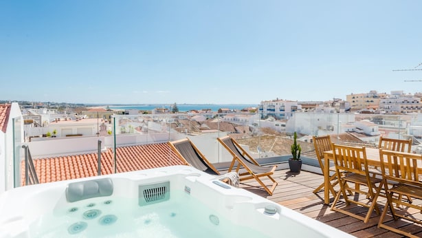 En takterrass med ett bubbelbad, trämöbler och utsikt över stadsbilden.
