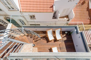 Terraza en la azotea con escalera espiral, cubierta de madera y dos sillones de descanso.