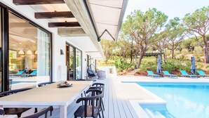 Uma área à beira da piscina com mesa e cadeiras, um espaço de estar coberto e uma piscina.