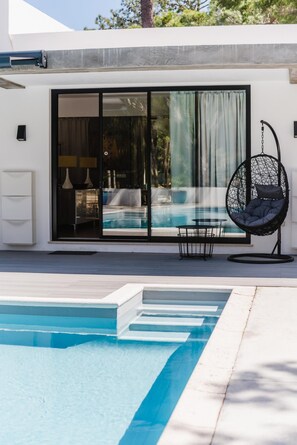 Ein moderner Poolbereich im Freien mit einer Hängematte, einem Tisch und Blick auf einen Pool sowie ein Gebäude mit großen Fenstern.