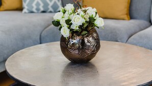 Uma sala de estar com um sofá, uma mesa de centro redonda e um vaso com flores.