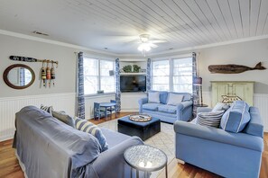 Experience the coastal charm in this nautical-themed living room, featuring a ceiling fan, large mirror, decorative bottles, striped curtain, and a wooden fish.