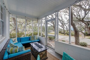 Relax in a cozy outdoor seating area with a sofa and fireplace, surrounded by large windows offering views of the surrounding trees.
