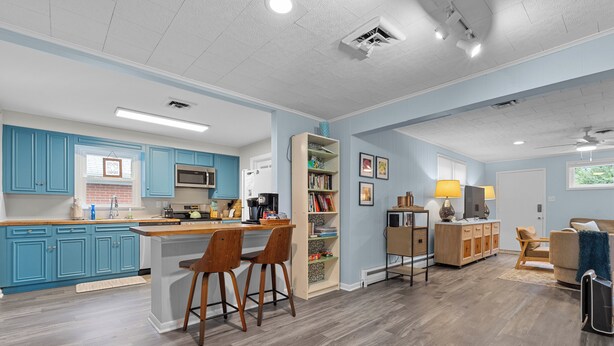 A modern kitchen with blue cabinets, a central island with stools, and a dining area with a sofa and lamp.