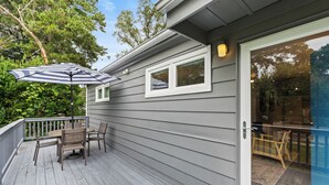 A wooden deck with a table and chairs, a striped umbrella, and a sliding glass door leading to an outdoor area.
