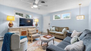 A living room with a ceiling fan, a flat-screen TV, two lamps, a sofa, a chair, and a coffee table.