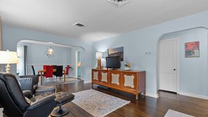 A modern living room with a leather sofa, a wooden entertainment center, and a dining area with red chairs.