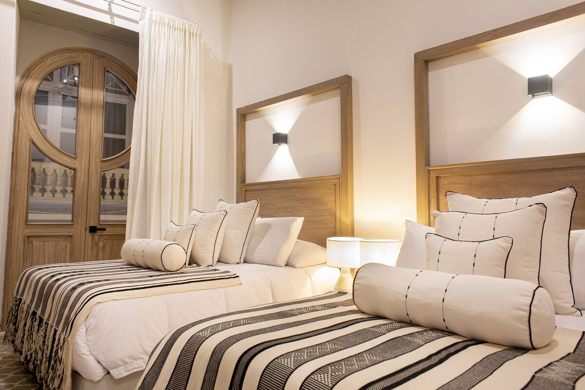 Een hotelkamer met twee bedden, een groot raam met gordijnen en wandlampen.