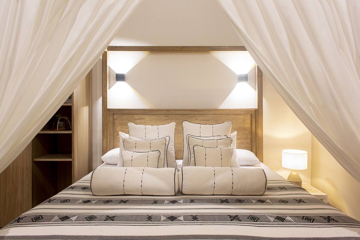 Een slaapkamer met een bed, gordijnen, een nachtkastje en een lamp.