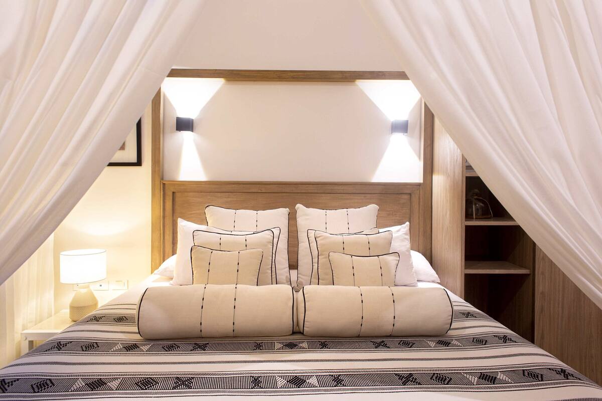 Een slaapkamer met hemelbed, nachtlampjes en een houten hoofdbord.
