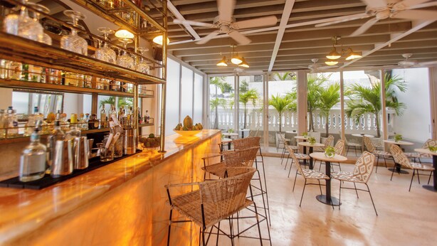 A bar area with wicker chairs, a bar counter with various bottles, and ceiling fans. - Sol de Alba Hotel Boutique (Cartagena)