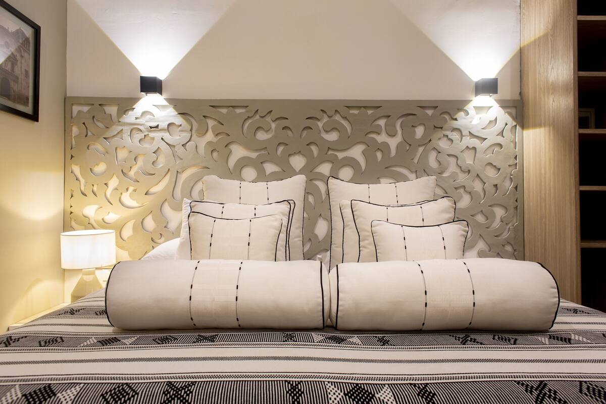 Een bed met een bedovertrek met een patroon, twee kussens en een decoratief hoofdbord met uitgesneden details.