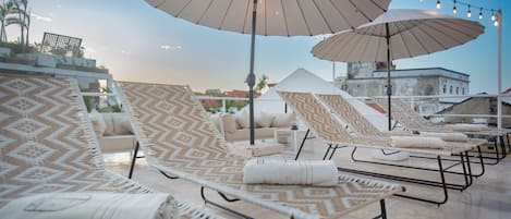A rooftop lounge area with patterned lounge chairs, large umbrellas, and string lights.
