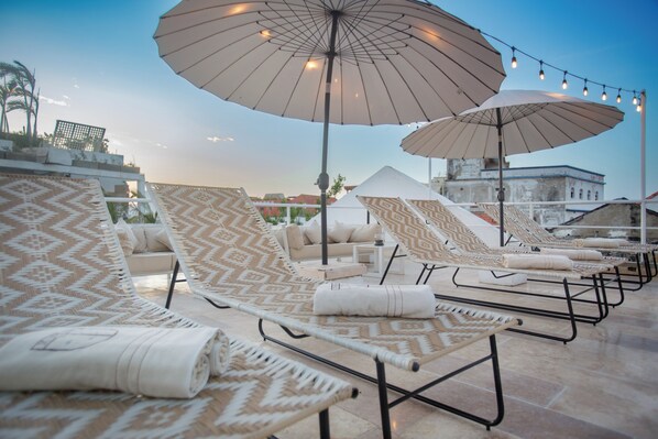 Een dakterras met gestoffeerde lounge fauteuils, grote parasols en lichtjes.